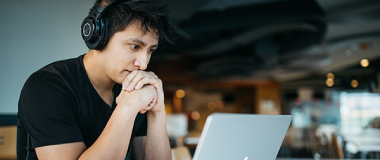 A man in a cafe with headphones on working on his laptop