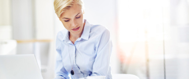 A woman in the office looking at a document while working on her laptop