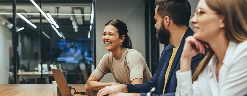 Three employees smiling while working in a team meeting