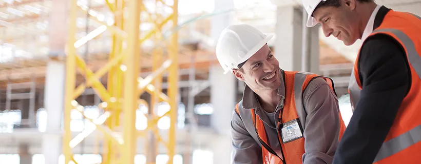 Two construction workers on site looking at blue prints