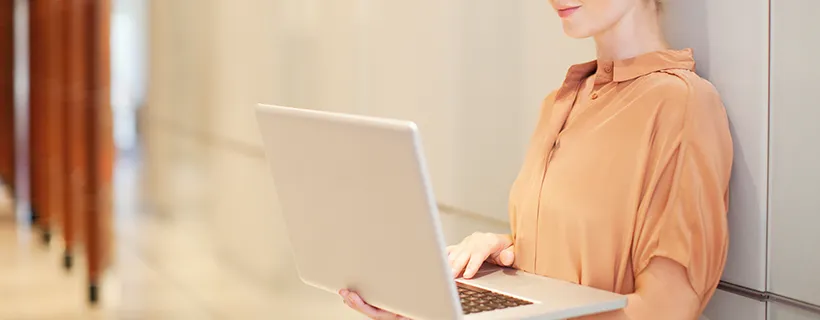 A woman standing up holding her laptop and working