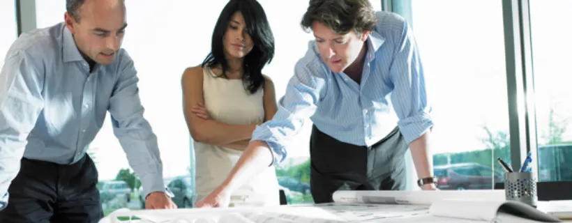 Three employees in a meeting room discussing a document