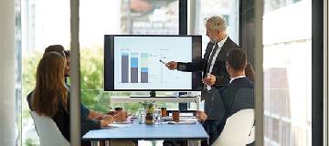 An employee leading a meeting and displaying charts and figures on a white board