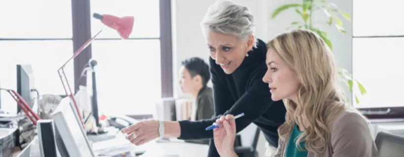 A manager working with her employee assisting her with work on the computer