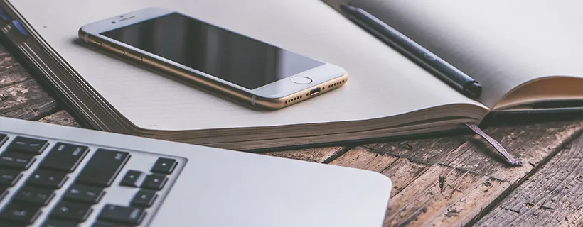 A phone on top of a notepad with a laptop on the desk