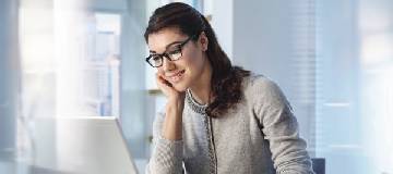 A woman sitting at her desk in the office working on her laptop