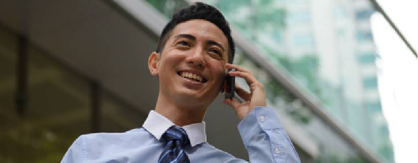 A man on the phone outside smiling and looking into the distance of the city