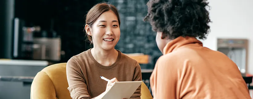 a woman taking notes talking to her colleague 