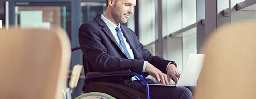 A man in a wheel chair in the office working on his laptop