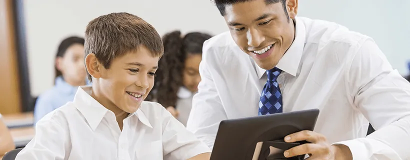 A mentor tutoring a young kid at school on a tablet device