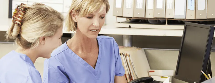 two healthcare workers looking at a report on a computer