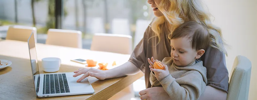 A mum holding her child while working on her laptop