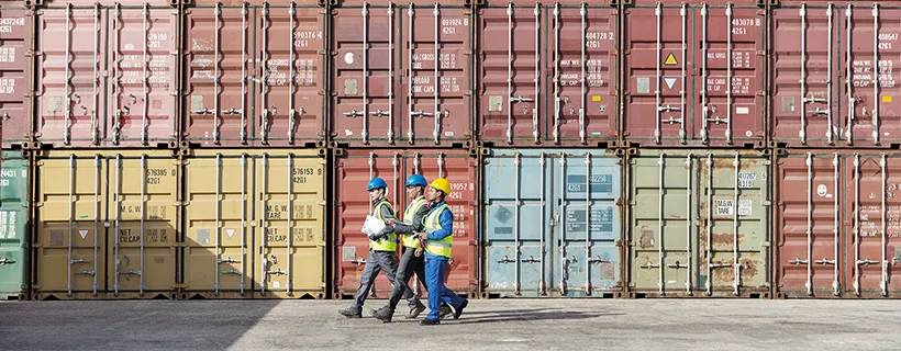 construction workers walking along side a wall of shipping containers