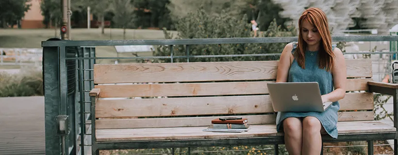 A woman sitting on a public bench working on her laptop