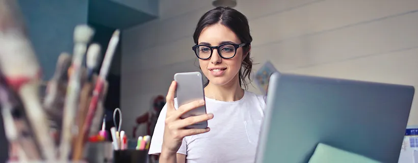 A woman on her phone in the office with her laptop in front of her