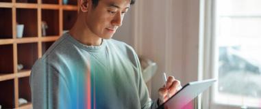 カジュアルな服装の男性が、明るい室内でスタイラスペンを使ってタブレットに集中して作業している様子。落ち着いた雰囲気の中でデジタル作業をしている印象。